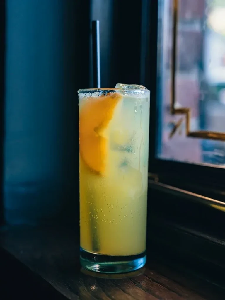 Tall glass of lemonade with ice, orange slice, and straw.