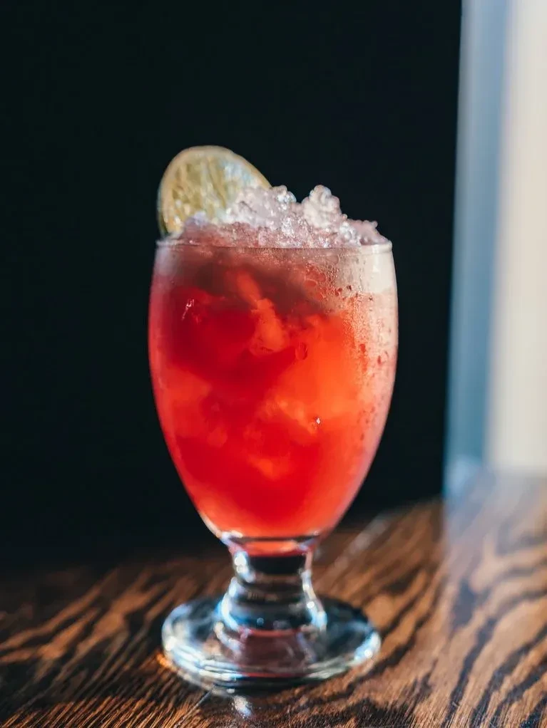 A red drink with crushed ice and a lime wedge.