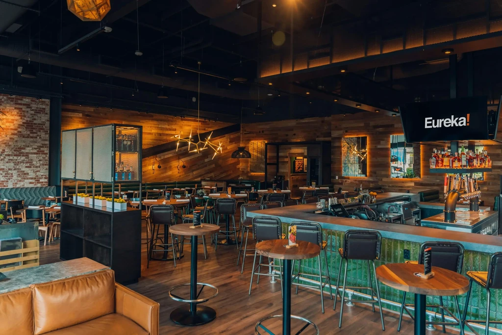 A modern restaurant with wooden walls, bar, tables, and a brown sofa.