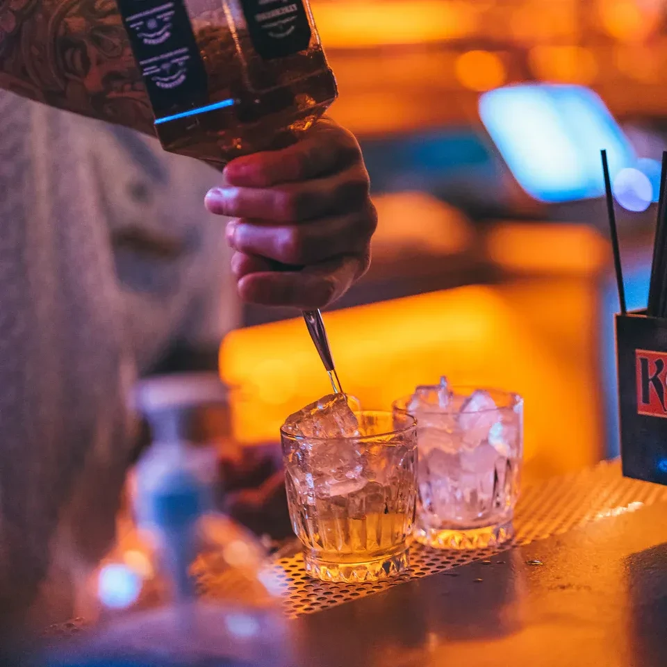 Bartender pours amber liquid into an ice-filled glass.