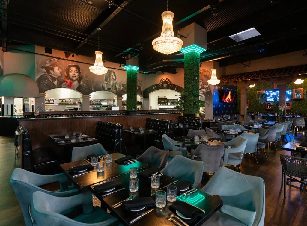 A spacious restaurant interior with murals, chandeliers, and elegant dining tables.