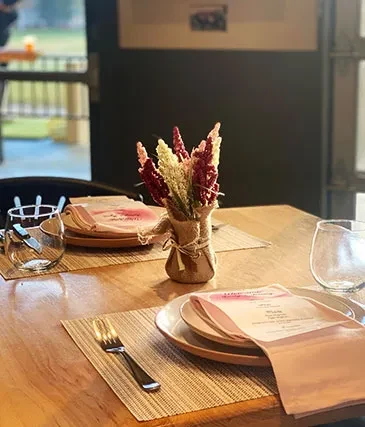 A rustic table set for two with pink menus and a small floral arrangement.