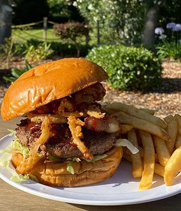 A loaded burger with onion rings, bacon, and a side of fries.