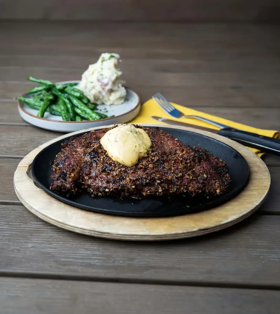 Steak with sauce, green beans, and potato salad on a wooden table.