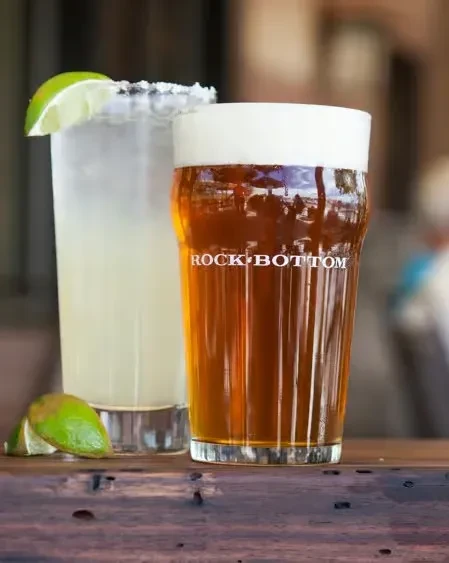 A beer and a margarita with lime on a wooden table.