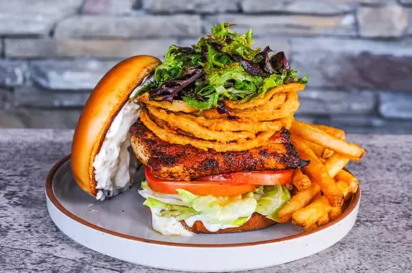 Spiced chicken sandwich with onion rings, lettuce, tomato, and fries.