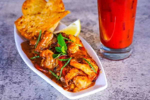 Shrimp scampi, garlic toast, and a Bloody Mary on a textured gray surface.