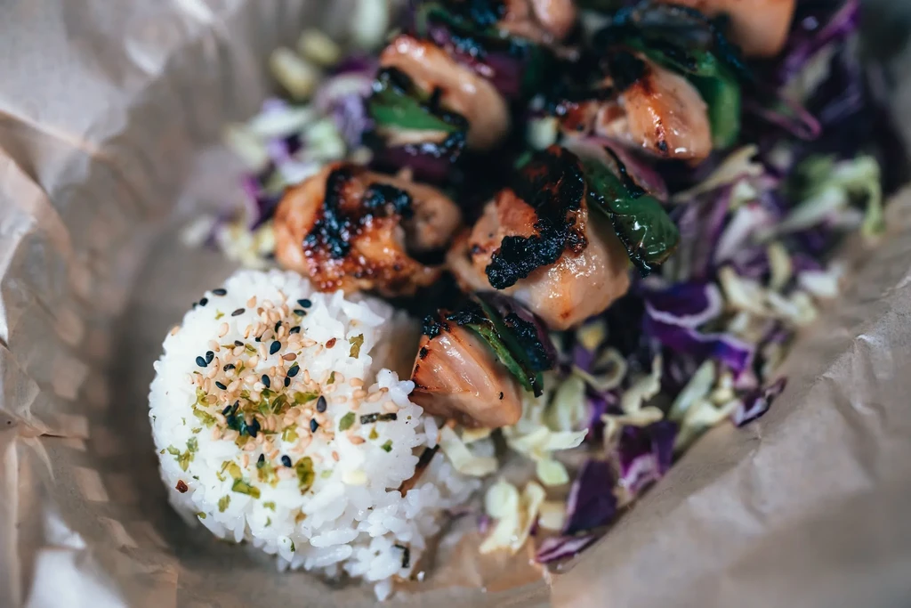 Teriyaki chicken skewers with white rice and cabbage in a brown paper bowl.