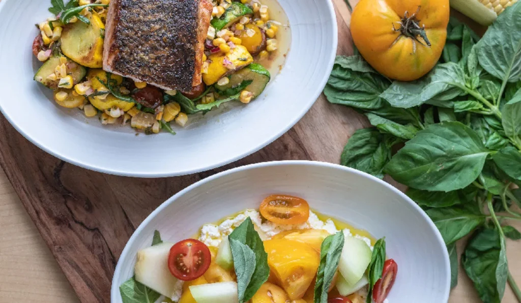 Two bowls of healthy food and fresh ingredients on a wooden board.