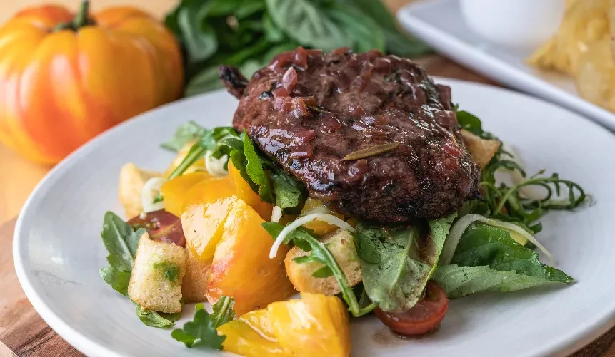 Steak with red sauce on a salad with orange tomatoes and croutons.