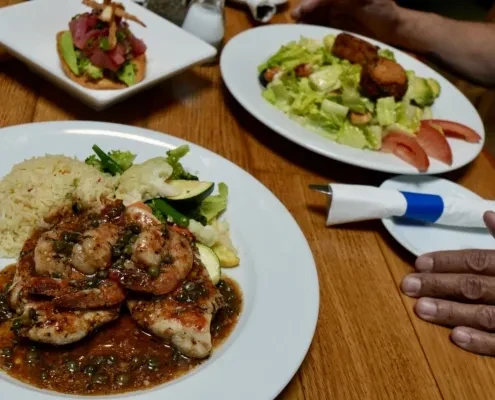 Three plates of food on a wooden table, with people's hands visible.