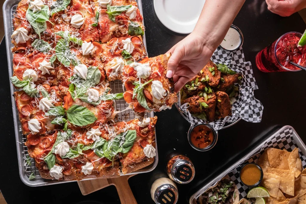 Hand grabbing a slice of pepperoni pizza topped with dollops of cheese.