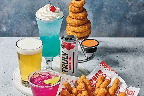 Table of fried appetizers, pink cocktail, blue drink, beer, and seltzer.