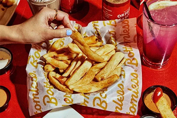 Hand picks fry from "Bottomless" basket; multiple sauces and pink drink.