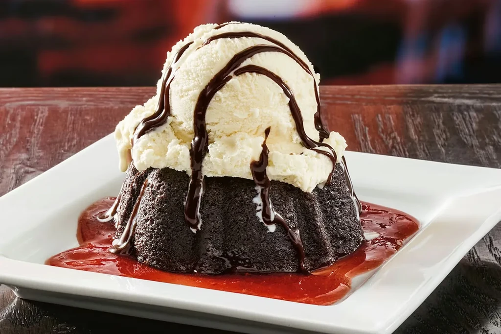 Chocolate lava cake topped with vanilla ice cream and red sauce.
