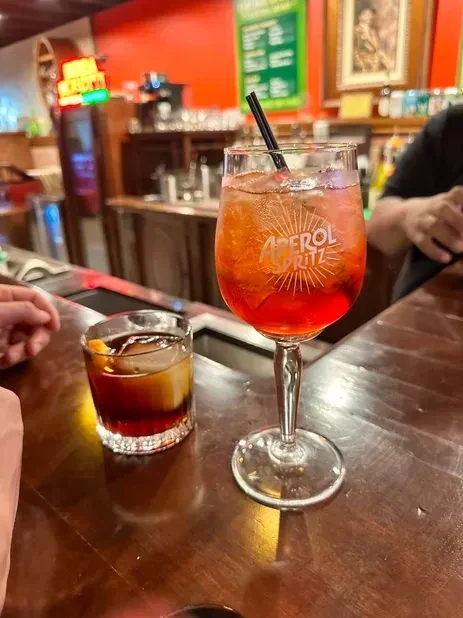 Two cocktails, an Aperol Spritz and an Old Fashioned, on a bar.