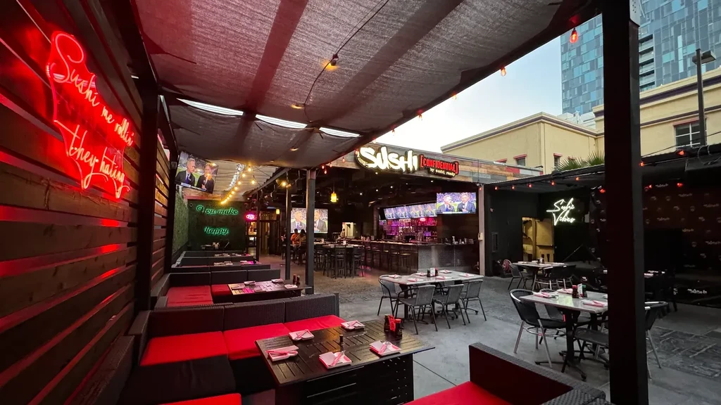 Sushi Confidential patio and bar with neon signs at dusk.