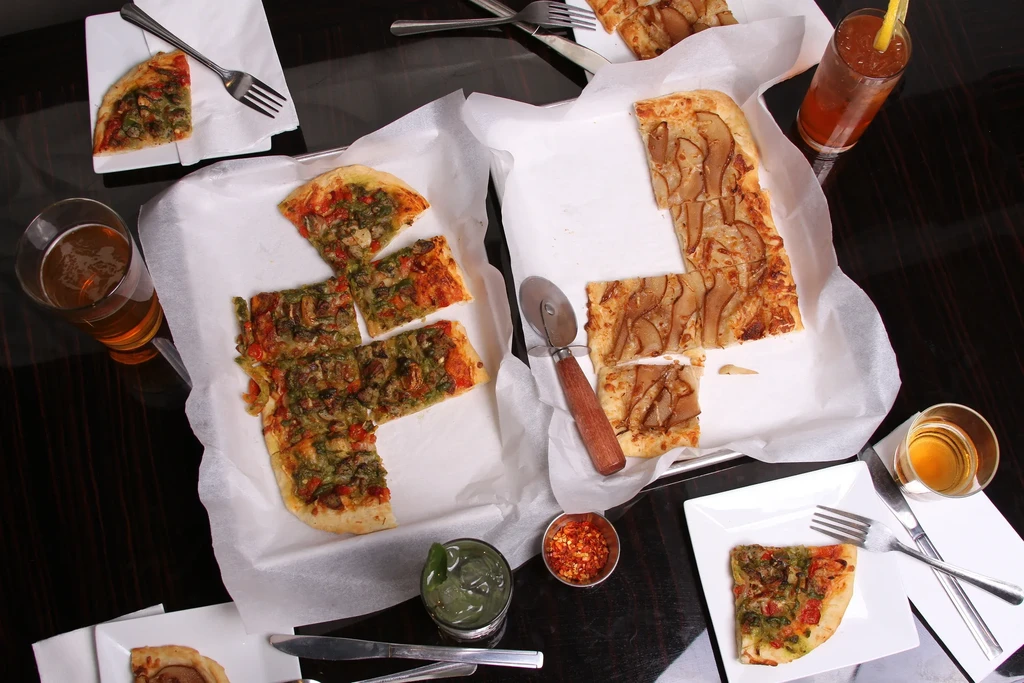 Overhead shot of two flatbreads with drinks and silverware on a table.