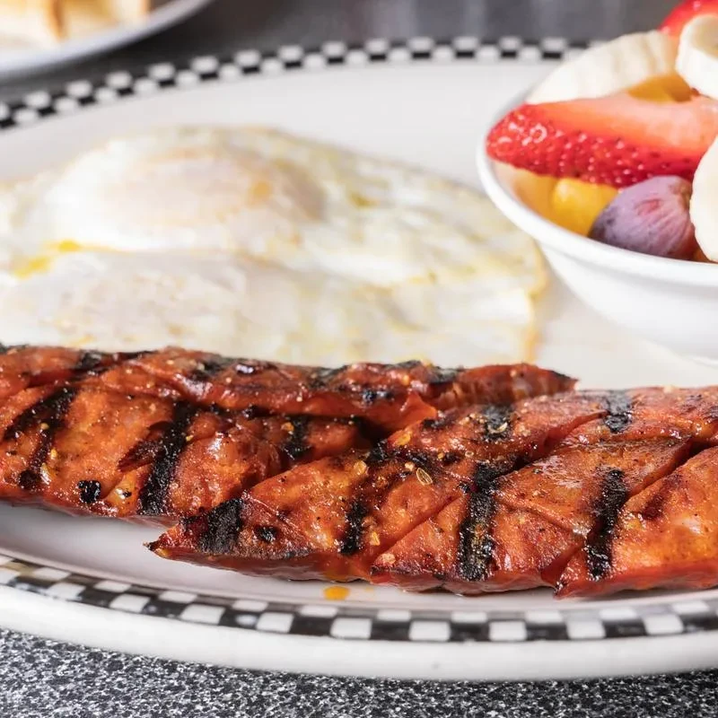 A breakfast plate with grilled sausage, fried eggs, and a fruit cup.