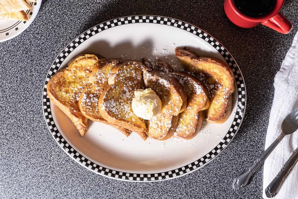 French toast with powdered sugar and butter on a black and white plate.