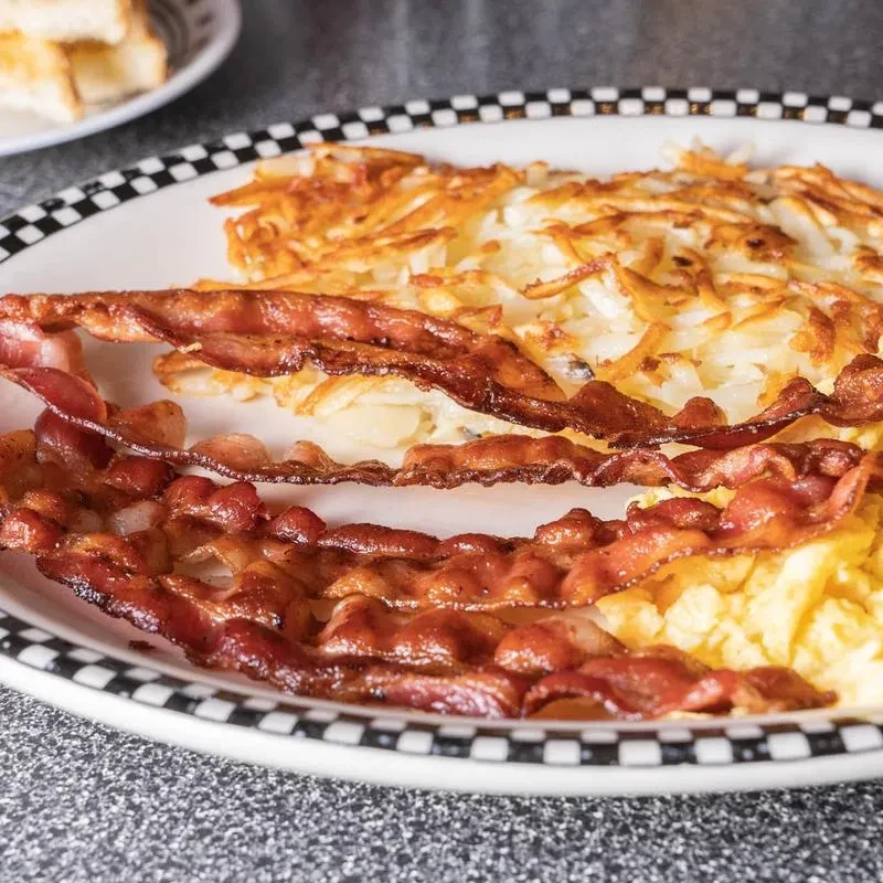 Bacon, hash browns, and scrambled eggs on a white plate.