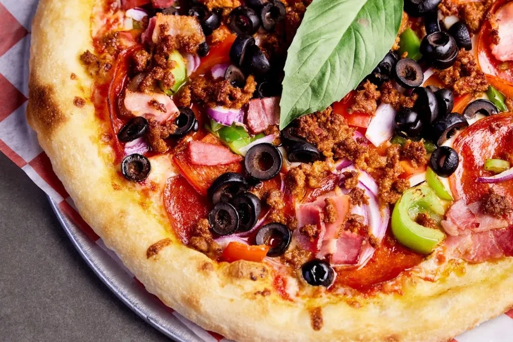 Close-up of a pizza with meat, pepperoni, olives, and vegetables.