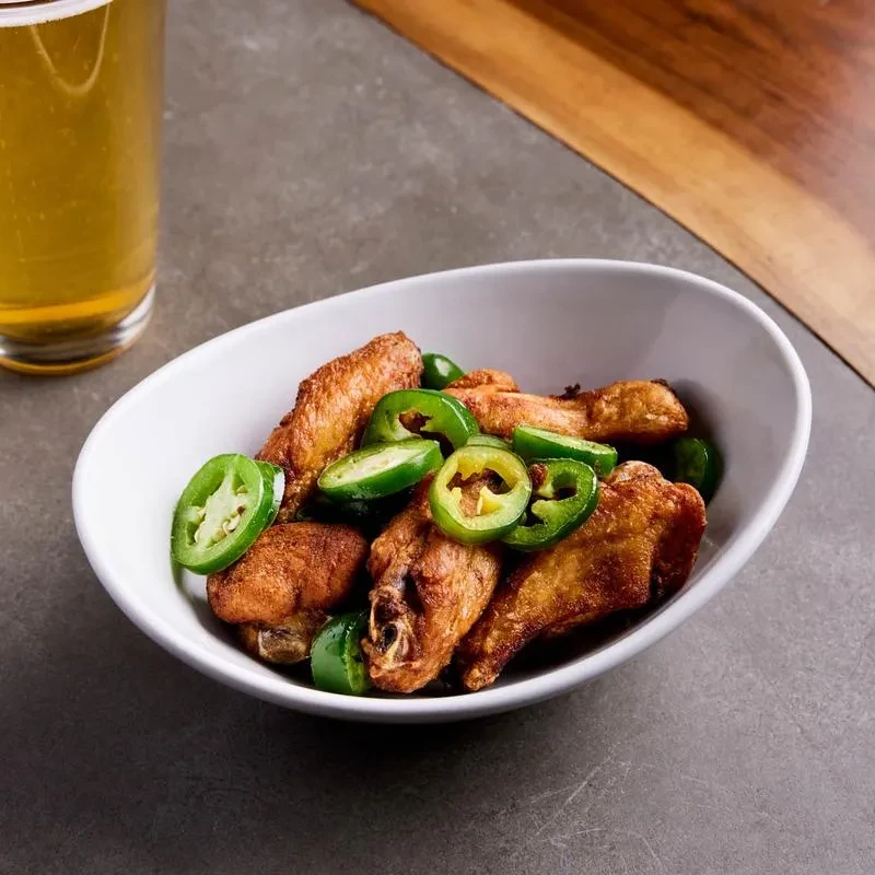 Crispy chicken wings with sliced jalapeños in a white bowl.