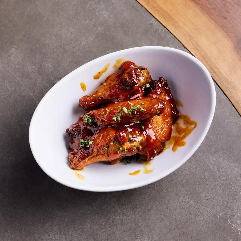 A white bowl holds several glossy, brown chicken wings with parsley.