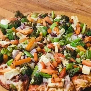 Close-up of a large pizza with broccoli, carrots, peppers, and cheese.
