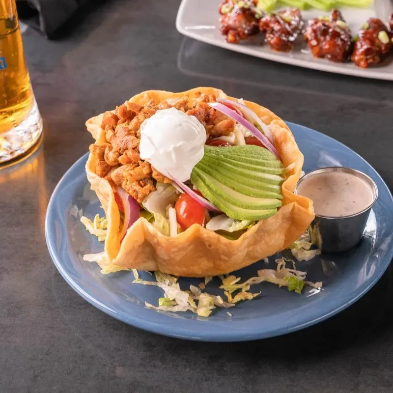 Taco salad in a crispy tortilla bowl with dressing and a drink.