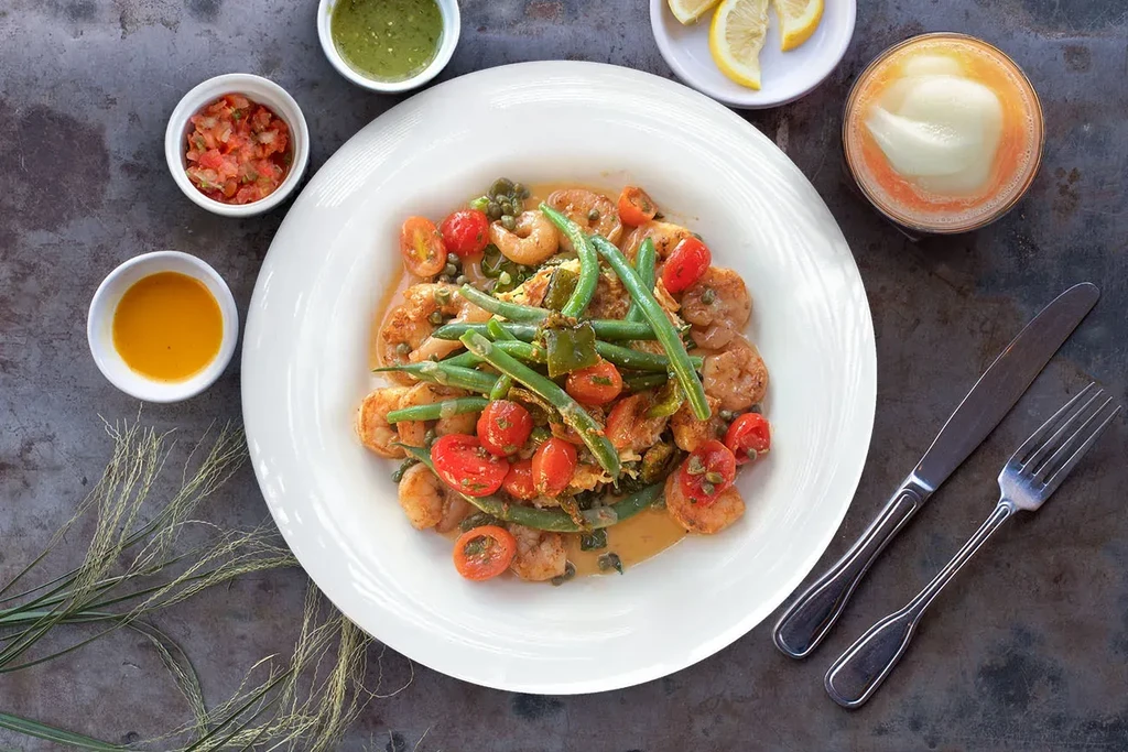 Shrimp, green beans, and cherry tomatoes in a white plate with sides.