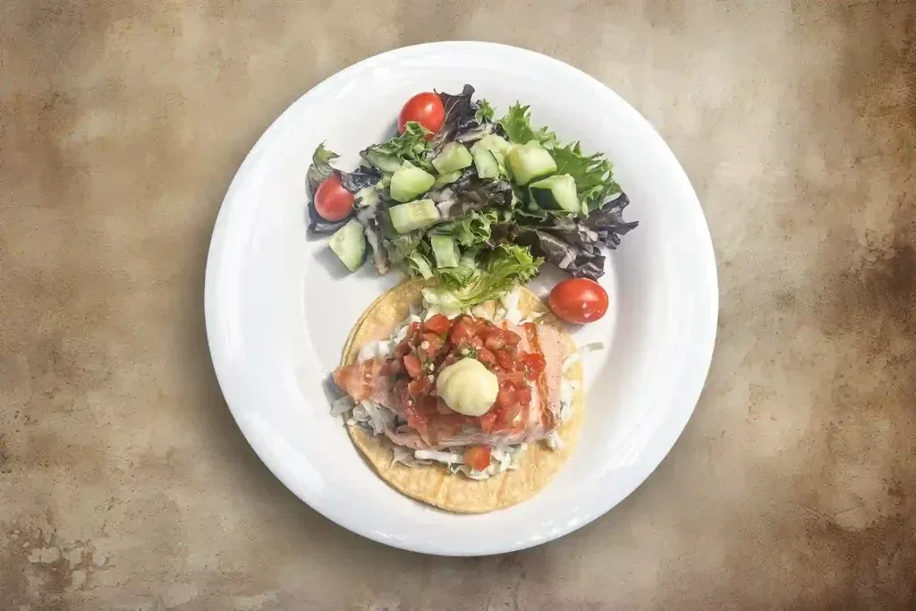 Overhead shot of a fish taco with a side salad on a white plate.