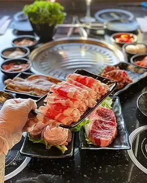 A hand presents thinly sliced rolled beef at a Korean barbecue.
