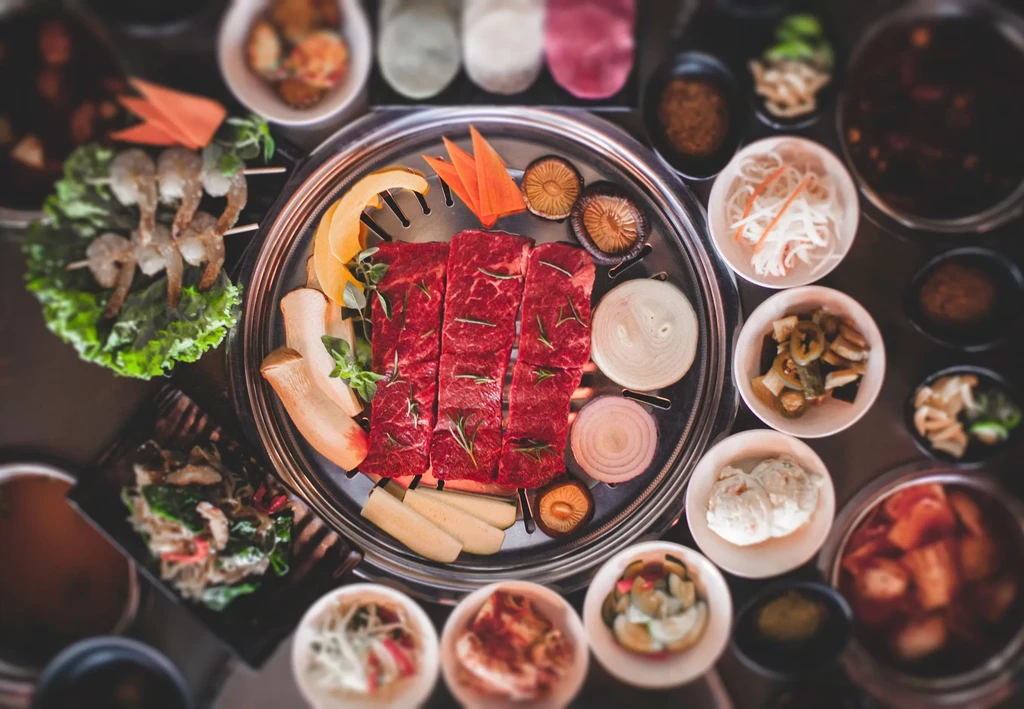 Korean BBQ grill with beef, mushrooms, onions, and many small side dishes.