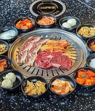 Korean BBQ grill with various cuts of meat and side dishes.