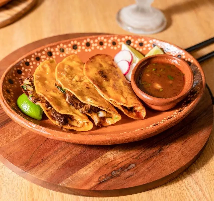 Birria tacos with a side of sauce on a terracotta plate.