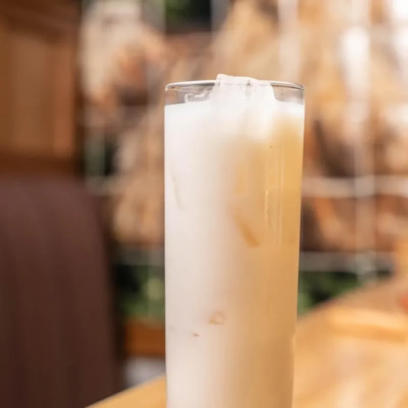 Tall glass of light-colored iced drink on a wooden surface.