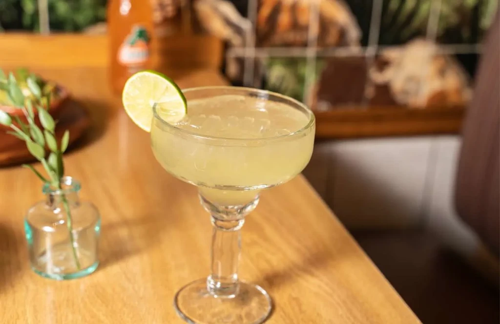A margarita with a lime slice on a wooden table.