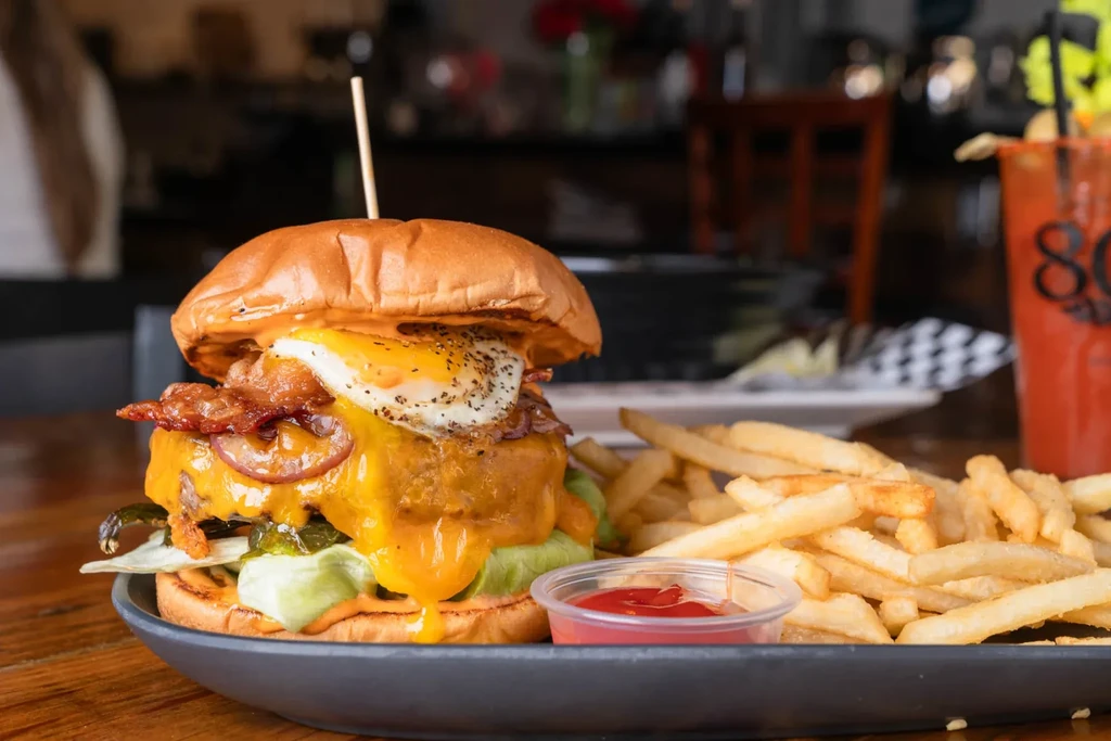 A burger with a fried egg, bacon, cheese, and fries on a plate.