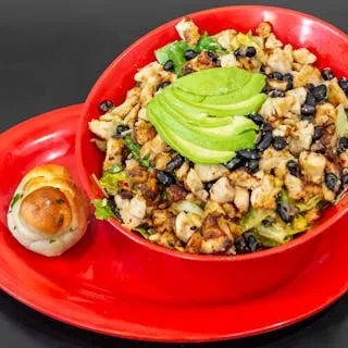 A bowl of chicken salad with black beans and avocado slices.