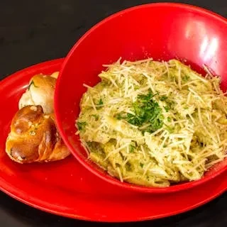 A red bowl of pesto pasta with grated cheese, next to garlic knots.