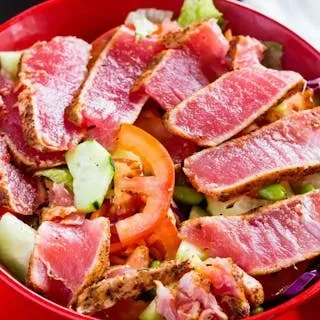 Seared tuna salad with sliced tomatoes and cucumber in a red bowl.