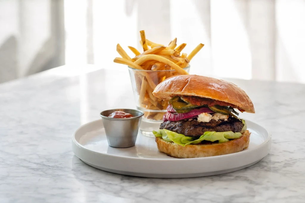 A burger, fries in a glass, and ketchup on a white plate.
