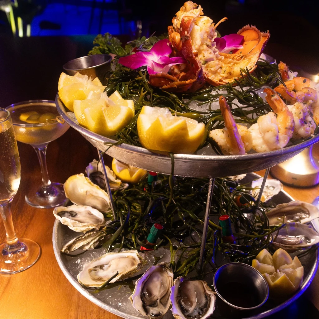 A two-tier seafood tower with lobster, shrimp, oysters, and lemon wedges.