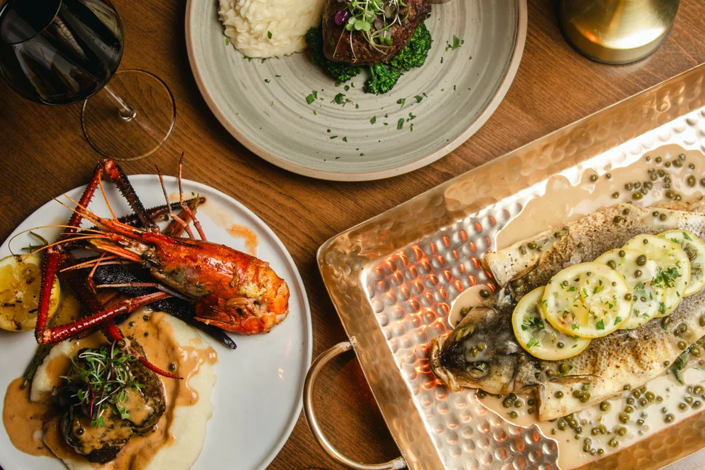 Seafood and steak dinner with wine and mashed potatoes on a wooden table.