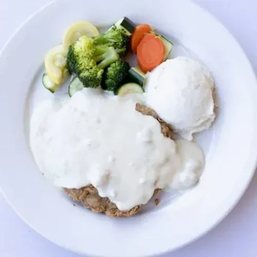 Chicken fried steak with mashed potatoes, gravy, and steamed vegetables.