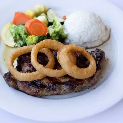 A plate of steak with onion rings, vegetables, and rice.