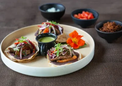Three tacos with meat, onions, and sauces on a round plate.