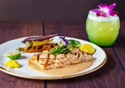 Grilled salmon, asparagus, carrots, and a green drink with a purple orchid.