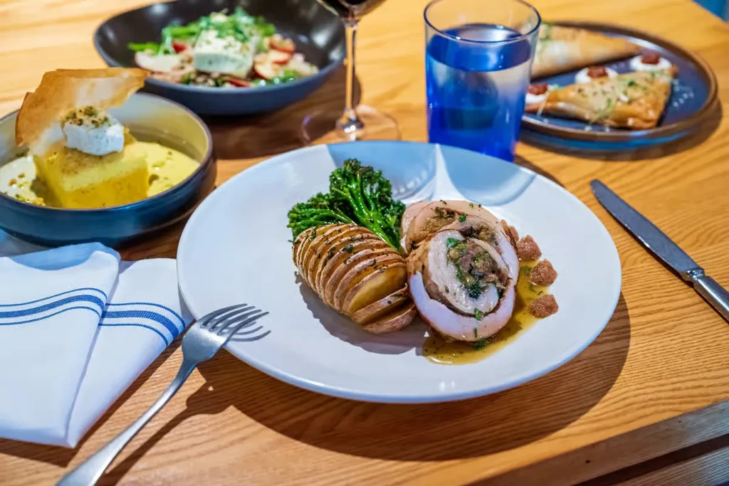 Dinner plate with stuffed chicken, sliced potatoes, broccoli, and other dishes.